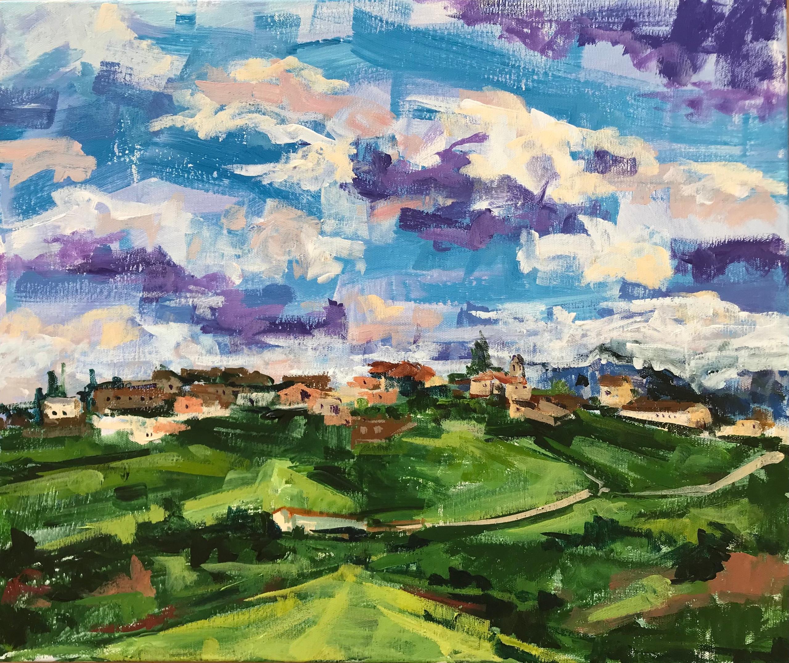 Pueblo en la línea del horizonte. Pradera verde con camino. Cielo con nubes.